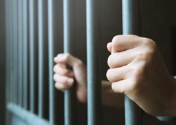 Man in prison hands of behind hold Steel cage jail bars. offender criminal locked in jail.